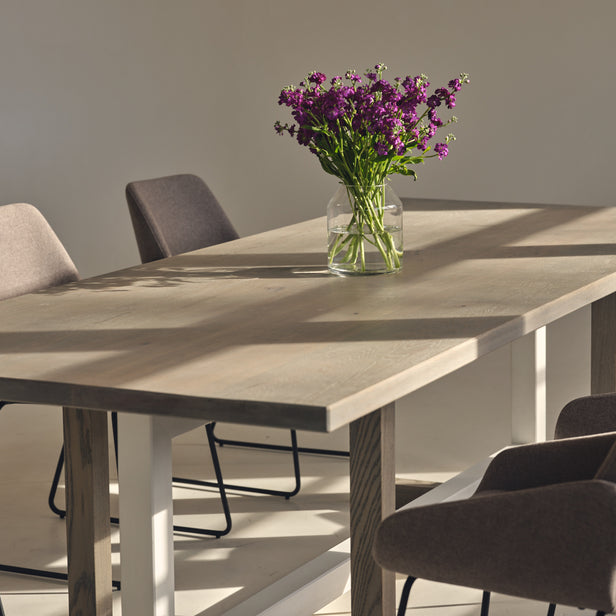 Custom made oak dining table with a modern geometric base, light grey finish, and a complimentary white trestle. 