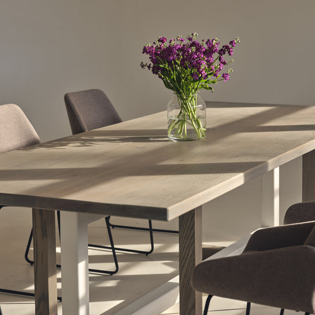 Custom made oak dining table with a modern geometric base, light grey finish, and a complimentary white trestle.